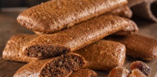 Was sind Printen? Gestapelte längliche braune Printen auf einem Holzbrett, mehrere gebrochen mit sichtbaren hellen Zuckerkristallen in der Krume, daneben brauner Kandiszucker