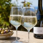 Zwei Gläser mit strohgelbem Prosecco und lebhaften Perlen auf einem sonnigen Tisch im Freien