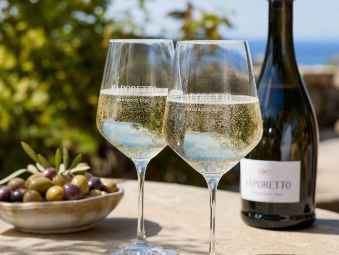 Zwei Gläser mit strohgelbem Prosecco und lebhaften Perlen auf einem sonnigen Tisch im Freien