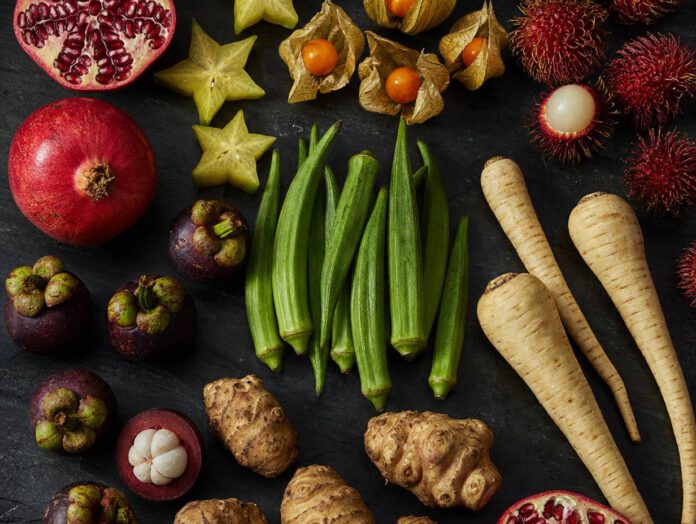 Exotische Früchte und Gemüse wie Granatapfel, Sternfrucht, Rambutan und Okra auf dunklem Schiefer angeordnet