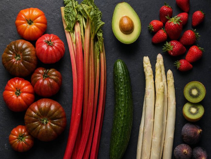 Tomaten, Rhabarber, Gurke, Spargel, Avocado, Erdbeeren, Kiwi und Feigen nebeneinander auf dunklem Schiefer