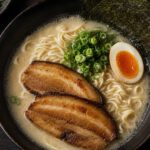 Schale Ramen von oben mit trüber heller Brühe, gewellten Nudeln, Schweinebauchscheiben, halbem Ei, Frühlingszwiebeln und Nori