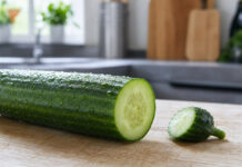 Warum schmeckt Gurke bitter? Angeschnittene Salatgurke auf einem Holzbrett, das abgetrennte Stielende liegt daneben
