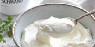 Wie schmeckt Schmand? Dicker weißer Schmand in einer rustikalen Keramikschale, ein Löffel hebt eine cremige Portion heraus