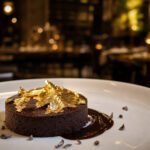Dunkles Schokoladendessert auf weißem Teller, belegt mit glänzendem essbarem Blattgold