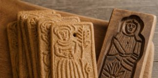 Was ist Spekulatius? Gefächerte rechteckige Spekulatius mit geprägten Figurenmotiven auf einem Holzbrett, daneben ein geschnitztes Holzmodel mit vertiefter Figur