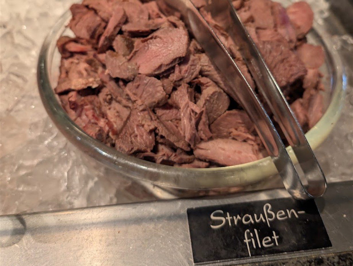 Aufgeschnittenes Straußenfilet in einer Glasschale auf Eis an einem Buffet, davor ein Schild mit der Aufschrift Straußenfilet