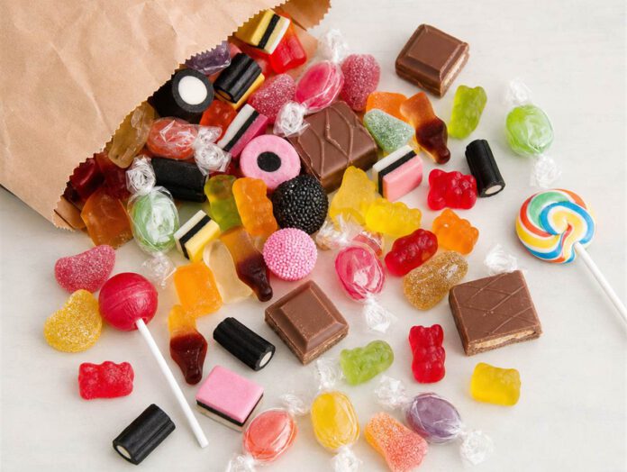 Bunte Bonbons, Gummibärchen, Lakritz, Schokoladenstücke und Lutscher auf einem hellen Tisch verstreut
