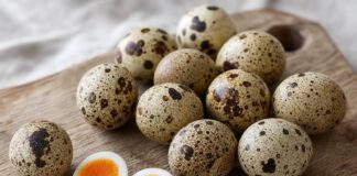 Wie schmecken Wachteleier? Wachteleier mit brauner Sprenkelung auf einem Holzbrett, zwei davon halbiert mit orangem Dotter