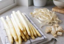 Warum schmeckt Spargel bitter? Frisch geschälte weiße Spargelstangen neben abgeschälten Schalen und abgeschnittenen Endstücken