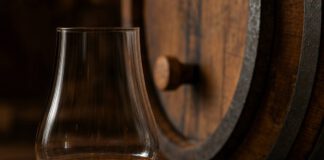 Internationaler Whisky-Tag: Herkunft, Regeln und Altersangaben Bernsteinfarbener Whisky in einem tulpenförmigen Nosingglas auf dunklem Holz, daneben eine Pipette mit einem Tropfen Wasser