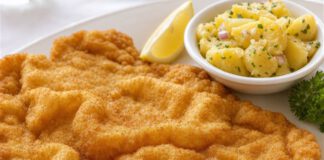Tag des Wiener Schnitzels: Warum nur Kalb so heißen darf Wiener Schnitzel mit goldgelber, gewellter Panade auf weißem Teller, daneben Zitronenspalte und Kartoffelsalat