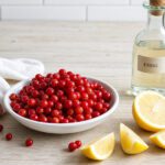 Kleine leuchtend rote Beeren in einer weißen Schale neben aufgeschnittenen Zitronenspalten