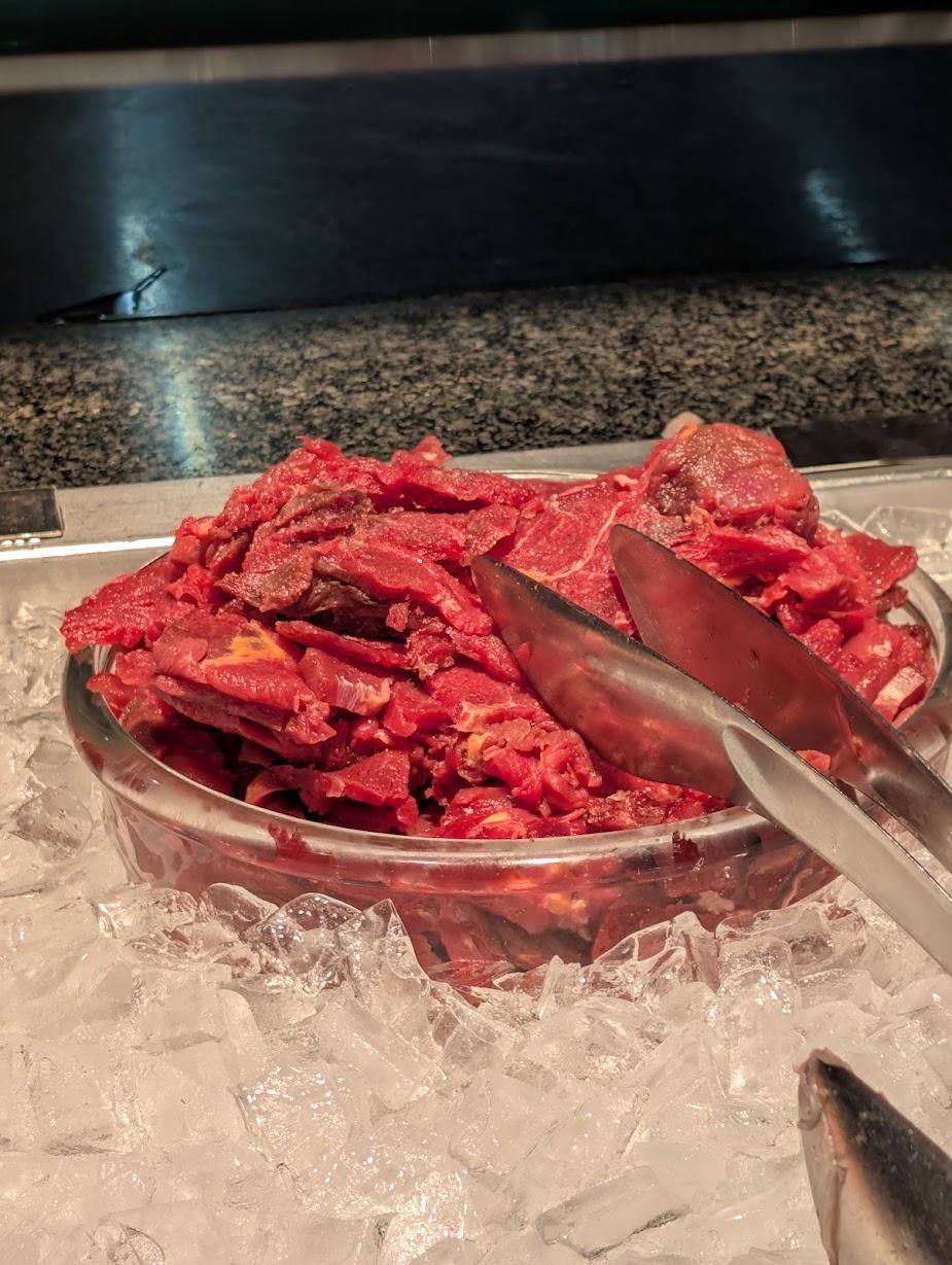 Hauchdünn aufgeschnittenes, dunkelrotes Fleisch in einer Metallschale auf Eis an einem Buffet