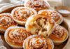 Tag der Zimtschnecke am 4. Oktober: Herkunft und Zimtfrage Frisch gebackene schwedische Zimtschnecken in Papierförmchen, bestreut mit Perlzucker, auf einem Holztablett