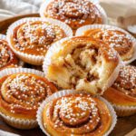 Frisch gebackene schwedische Zimtschnecken in Papierförmchen, bestreut mit Perlzucker, auf einem Holztablett