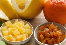 Orangeat und Zitronat: Was ist der Unterschied? Zwei Schalen nebeneinander, links helle Würfel Zitronat, rechts bräunlich-orange Würfel Orangeat, dahinter eine dickschalige Zitrusfrucht und eine Orange