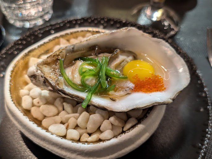 Rohe Auster in der Schale mit Eigelb, orangefarbenem Tobiko-Rogen und Frühlingszwiebel