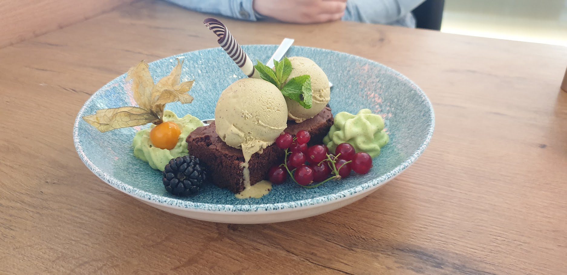 Brownie mit zwei Kugeln Pistazieneis, Pistaziencreme, Physalis und roten Johannisbeeren