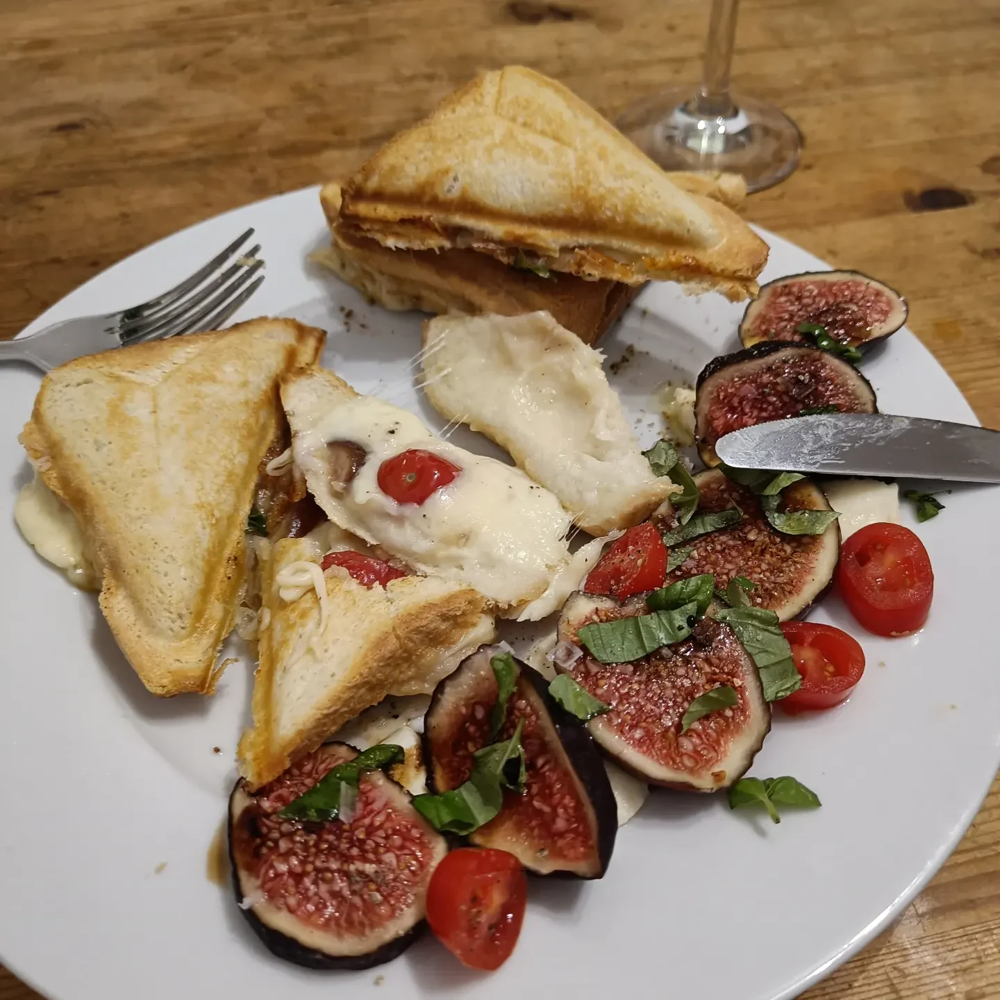 Getoastete Sandwiches mit geschmolzenem Mozzarella neben Feigen und Tomaten