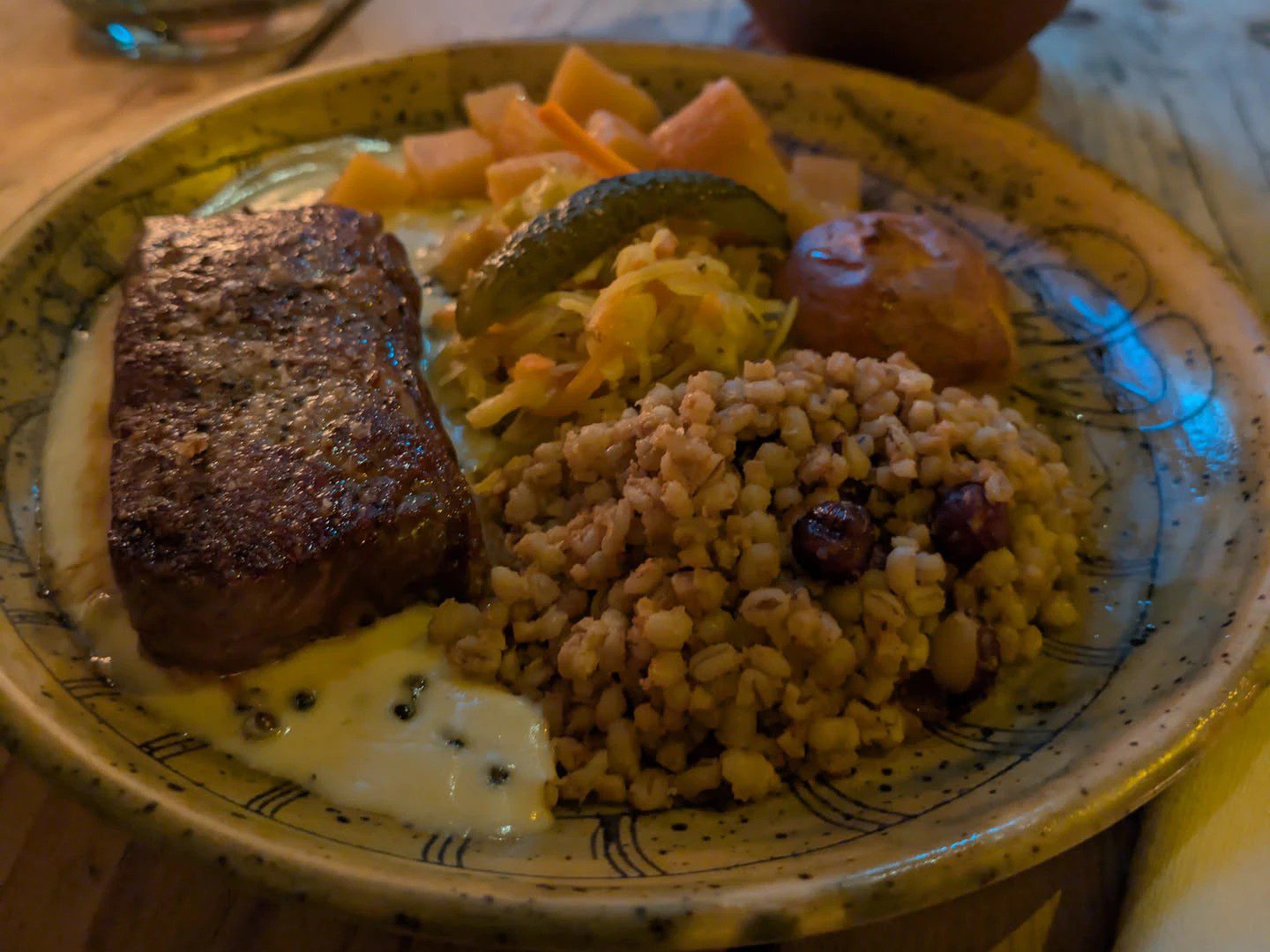 Teller mit gebratenem Steak, Graupen mit dunklen Beeren, Krautsalat, Essiggurke und einem kleinen Brötchen