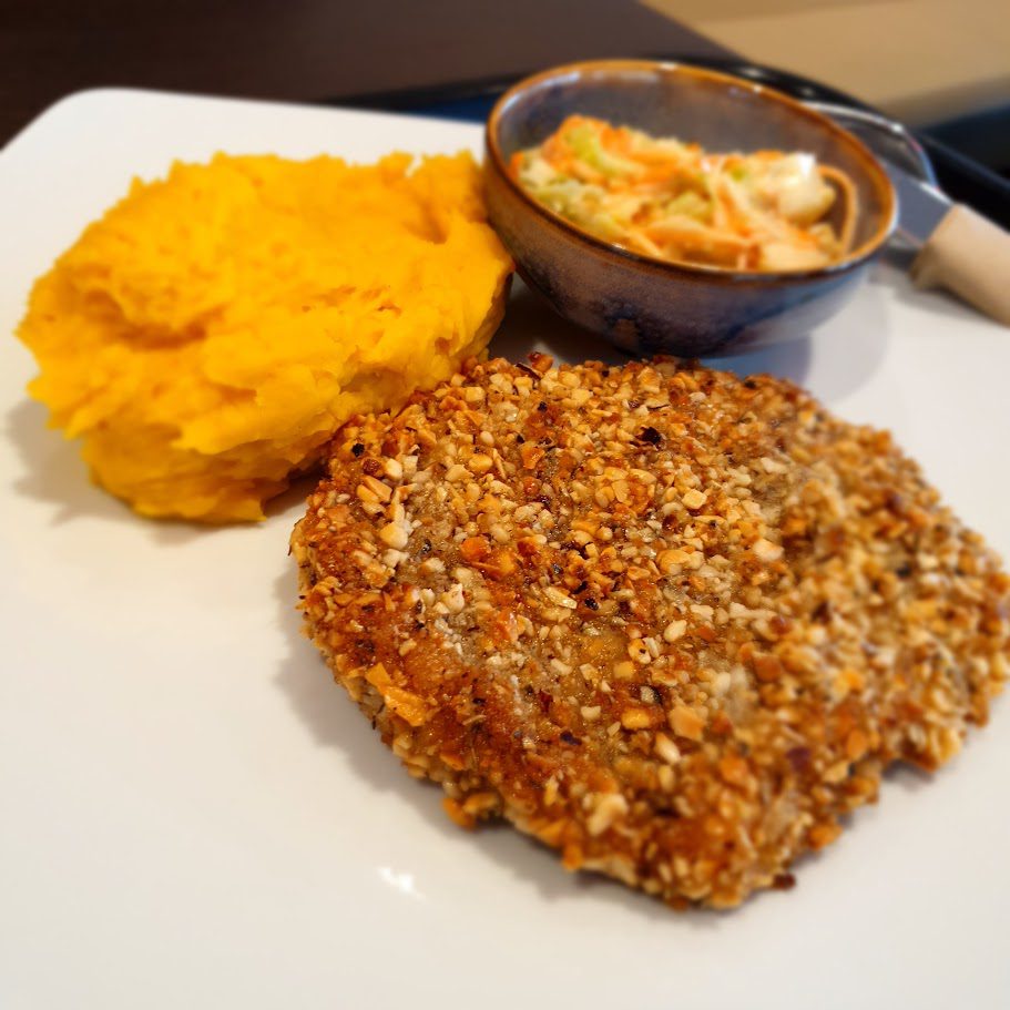 Orangefarbenes Kürbispüree neben einem Schnitzel mit Nusskruste und einem Schälchen Krautsalat