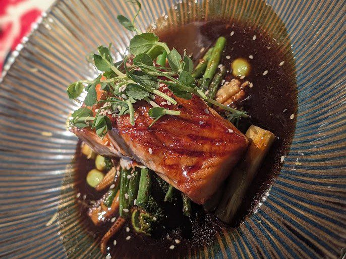 Teriyaki-glasiertes Lachsfilet in dunkler Sauce mit Babymais, grünen Bohnen und Sesam
