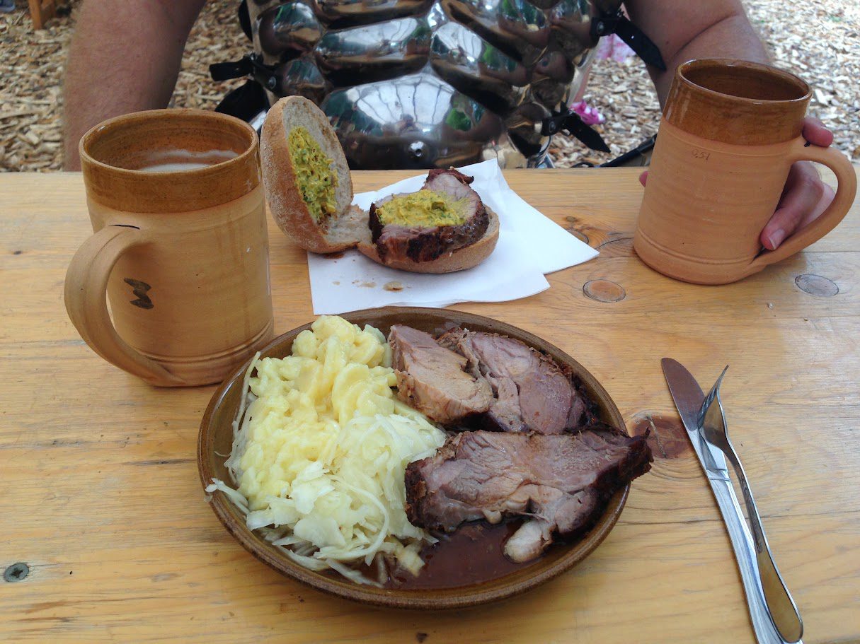 Teller mit Schweinebraten, Sauerkraut und Käsespätzle auf einem Mittelaltermarkt, dazu Tonkrüge