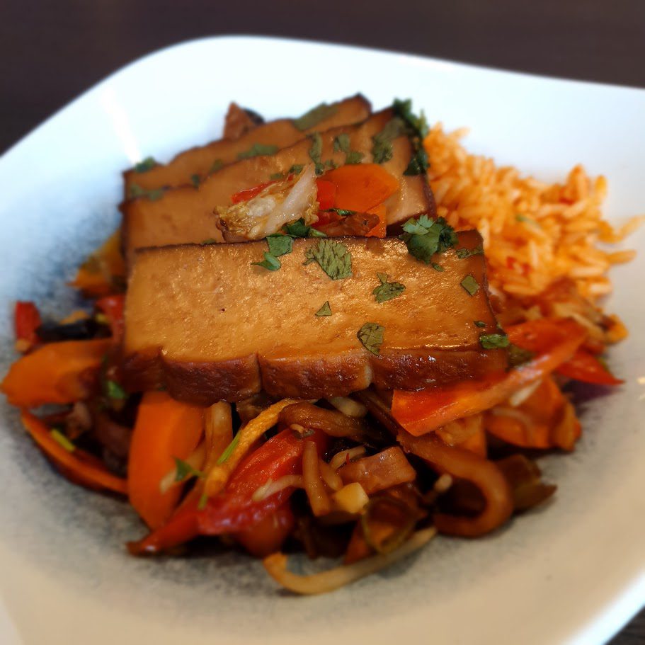 Scheiben Räuchertofu auf Wokgemüse mit Paprika und Karotten, daneben Tomatenreis