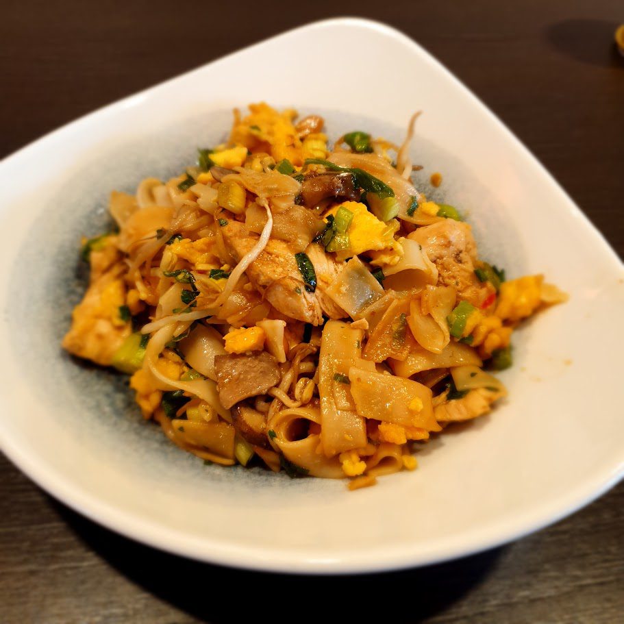 Gebratene breite Reisnudeln mit Hähnchen, Ei, Sojasprossen und Frühlingszwiebeln
