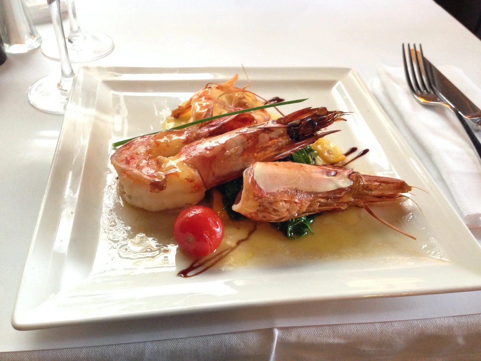 Längs halbierte Riesengarnelen in der Schale auf Blattspinat, mit Kirschtomate und Balsamicoreduktion auf weißem Teller