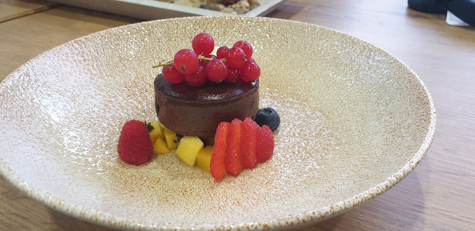 Schokoladentörtchen mit roten Johannisbeeren, Mangowürfeln und aufgefächerter Erdbeere auf hellem Teller