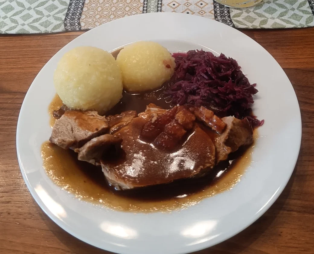 Zwei Kartoffelklöße neben Braten mit dunkler Sauce und Blaukraut
