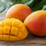 Reife Mango, im Würfelmuster aufgeschnitten, neben ganzen Früchten