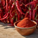 Rotes Paprikapulver in einer Schale, getrocknete Paprika dahinter