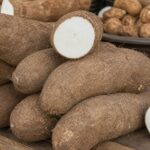 Große Yamsknollen an einem Marktstand, eine aufgeschnitten